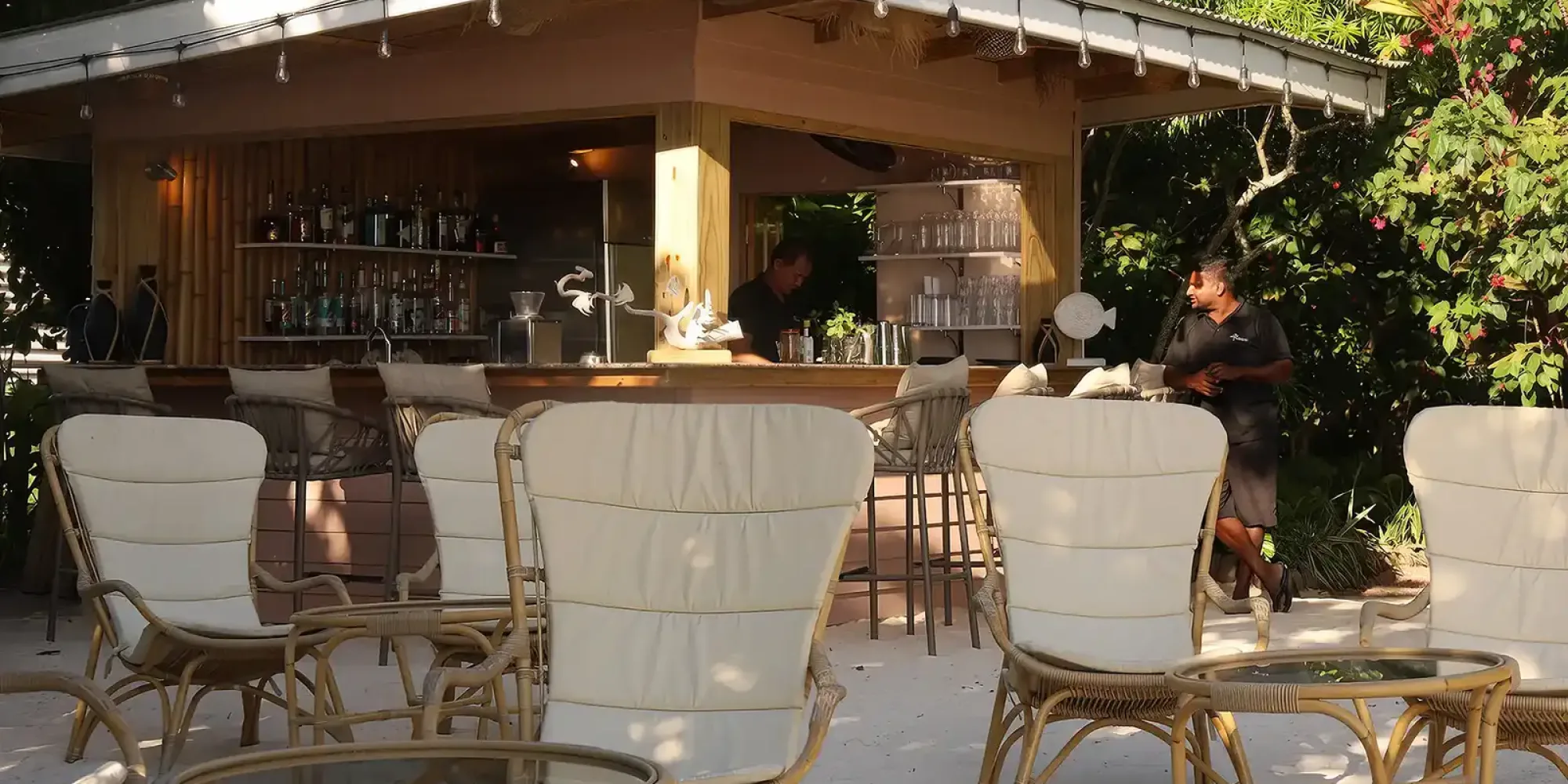 Outdoor Bar, Le Repaire Boutique Hotel and Restaurant, Seychelles consisting of lounge chairs in rattan and coffee tables with glass top and rattan structure.